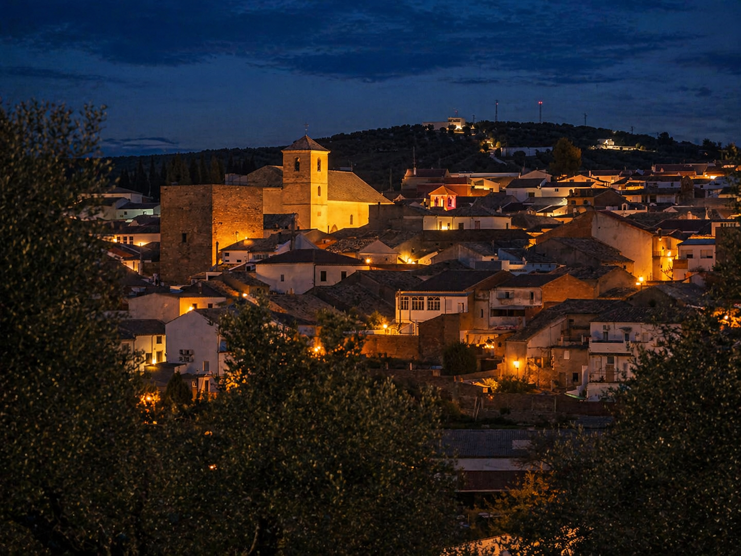 Begíjar al anochecer — torre iluminada sobre los tejados